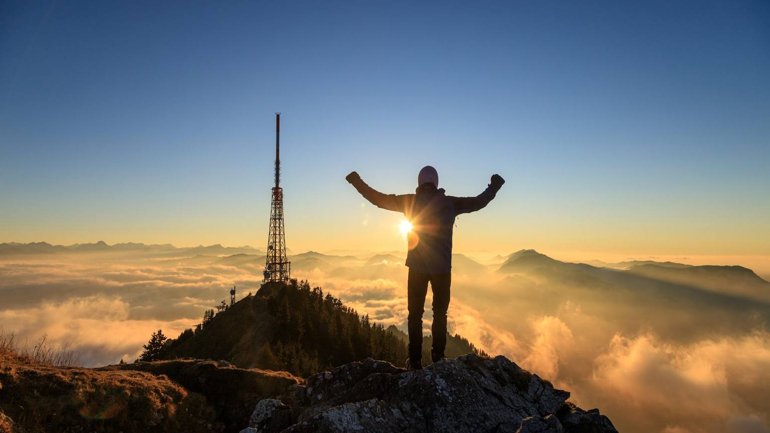 Wanderer auf dem Gipfel des Grünten bei Sonnenaufgang, dahinter der Sendemast über dem Nebelmeer