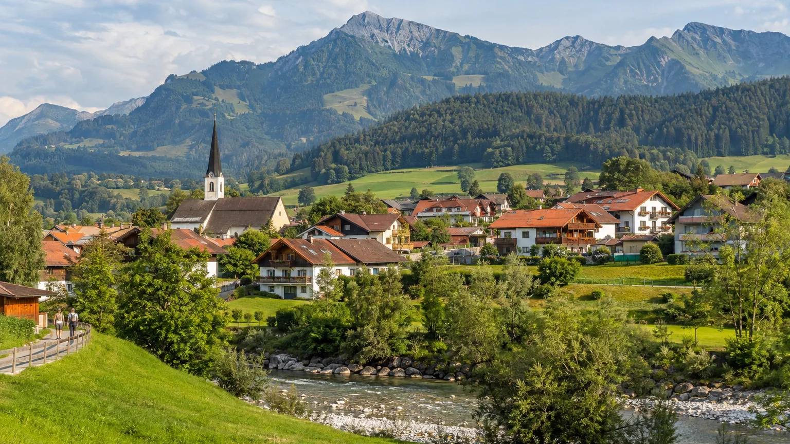 Blaichach im Oberallgäu mit Kirche und Häusern an der Iller, dahinter die Berge des Naturparks Nagelfluhkette