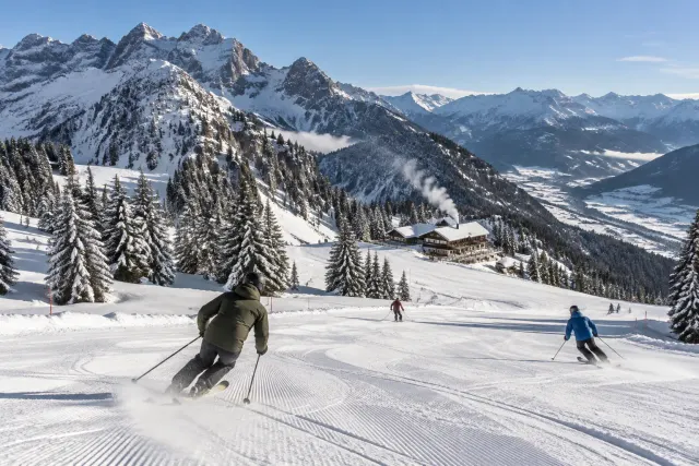Skifahrer auf einer frisch präparierten Piste im Allgäu, verschneite Tannen und Gipfel unter blauem Himmel