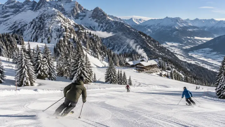 Skifahrer auf einer frisch präparierten Piste im Allgäu, verschneite Tannen und Gipfel unter blauem Himmel