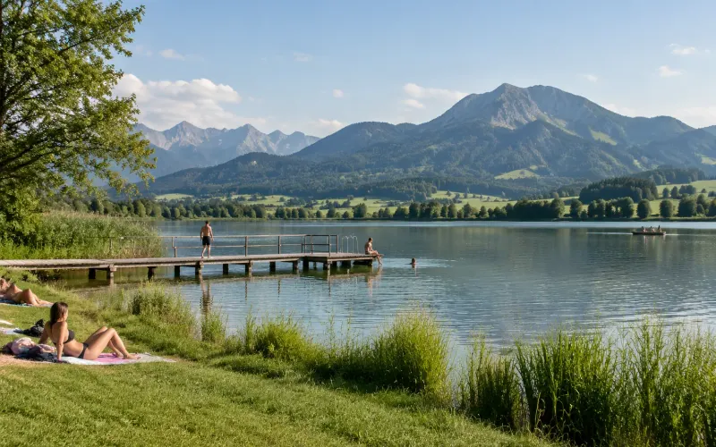 Niedersonthofener See mit Badesteg und Liegewiese, Badegäste am Ufer, dahinter der Grünten