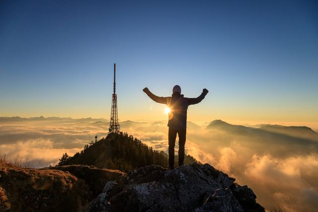 Person mit erhobenen Armen auf dem Grünten-Gipfel bei Sonnenuntergang über dem Allgäu