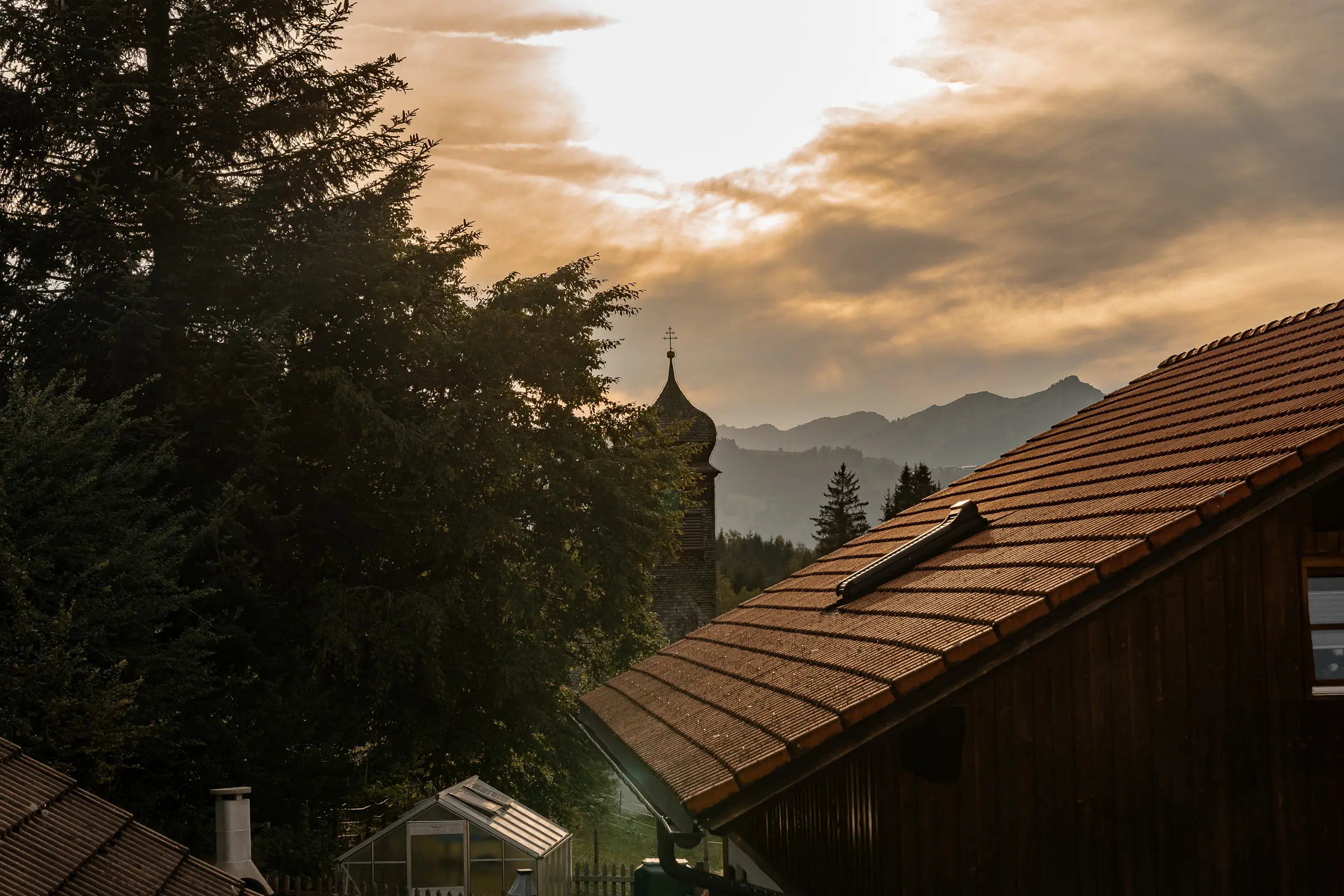 Abendstimmung vom Balkon der Ferienwohnung Auszeit Berg Nest in Imberg: Dächer, Kirchturm und die Allgäuer Berge im Gegenlicht