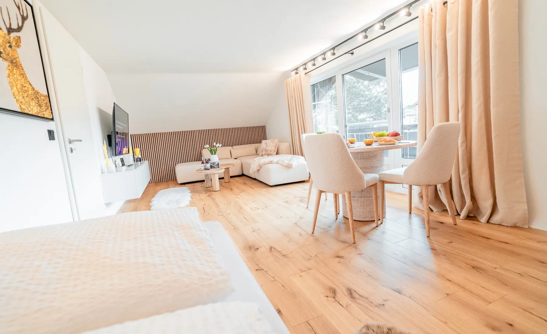Heller offener Wohn- und Essbereich der Ferienwohnung Bergblick in Sonthofen mit Flatscreen-TV, Ecksofa, Esstisch und großzügigem Balkonzugang