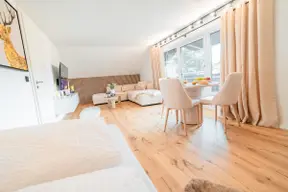 Heller offener Wohn- und Essbereich der Ferienwohnung Bergblick in Sonthofen mit Flatscreen-TV, Ecksofa, Esstisch und großzügigem Balkonzugang